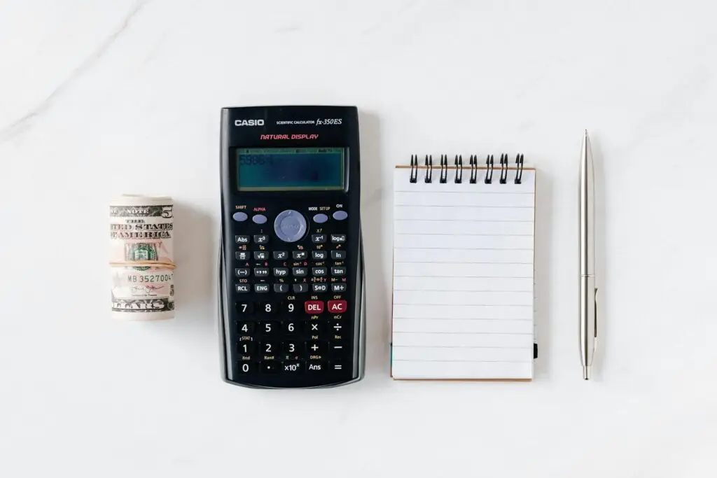 Home 12 Top view of financial tools including a calculator, notepad, pen, and rolled cash on a white background.