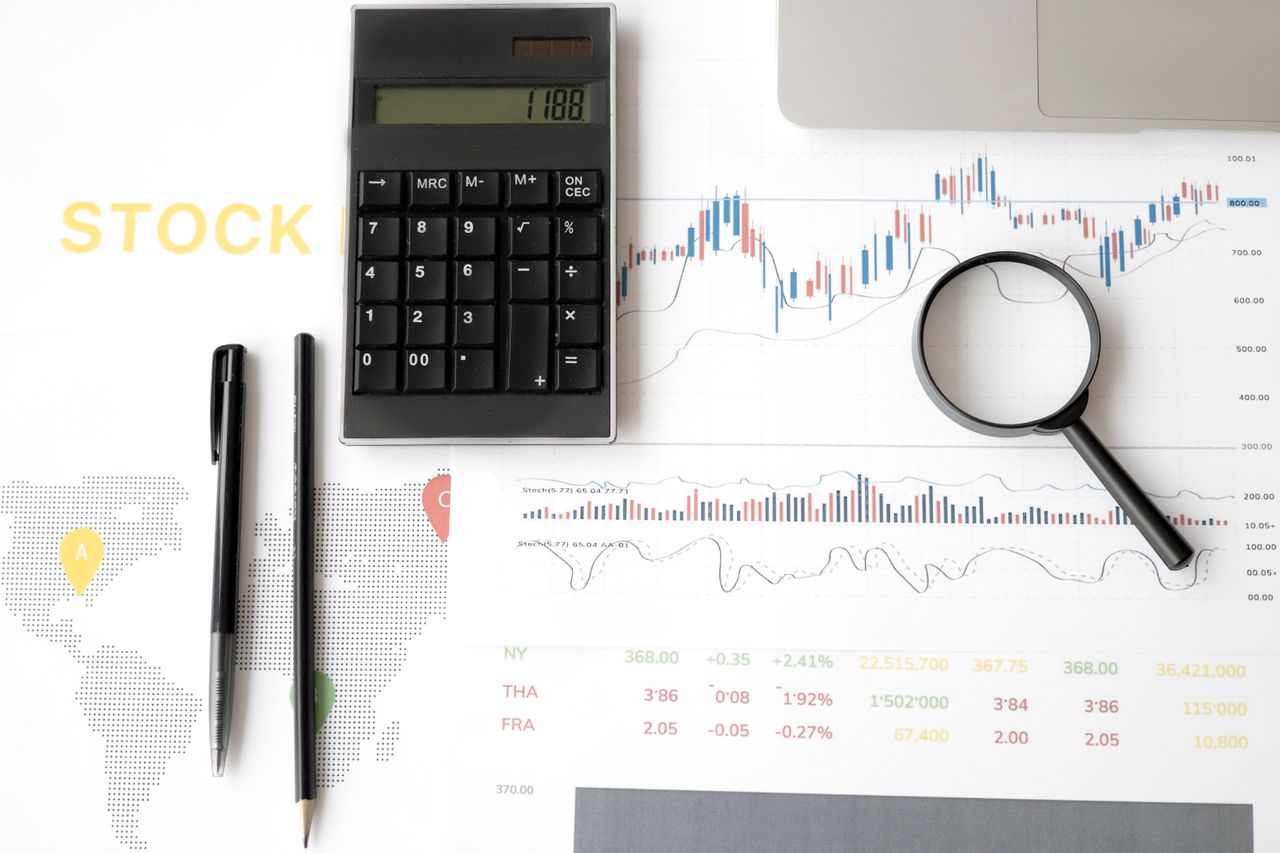 about-us Flat lay of stock market analysis tools including calculator, graphs, and magnifying glass.