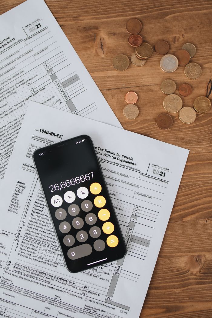 services-03 Calculator displaying number placed on tax forms with scattered coins on wooden desk.